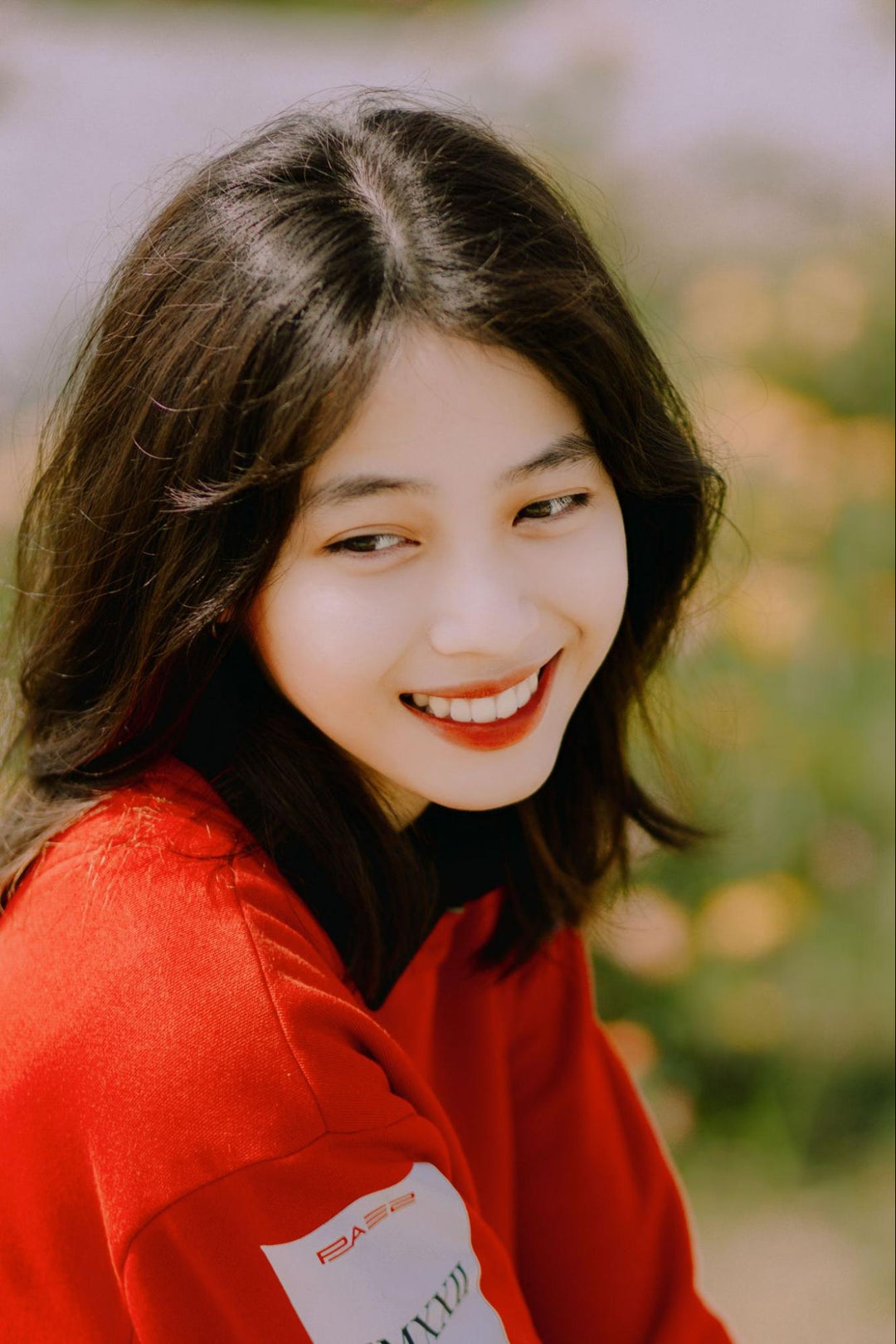 A smiling woman with good skin in a red top.